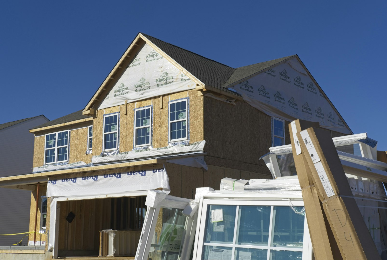 A house under construction with plywood walls and stacked windows in the foreground